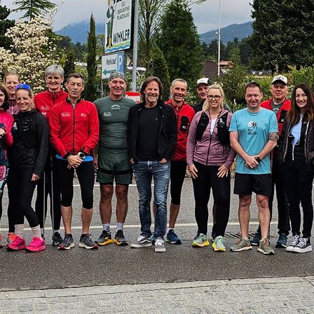 Eine Gruppe von Läufern in Sneakers und Jacken steht lächelnd in einer Reihe auf der Straße.