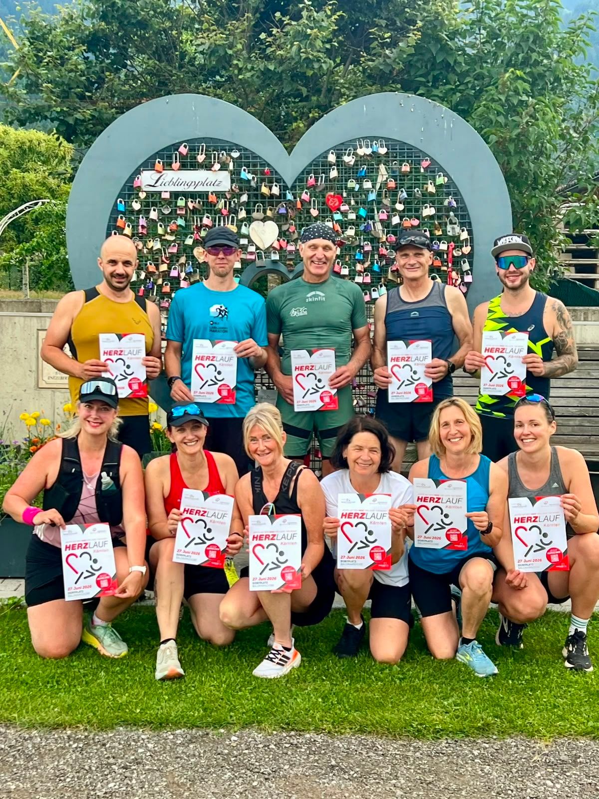 Eine Gruppe von Menschen posiert für ein Foto, während sie Zertifikate mit den Worten Herzlauf in der Hand halten. Sie tragen alle Laufbekleidung und lächeln. Dahinter ist eine Wand mit vielen Vorhängen.