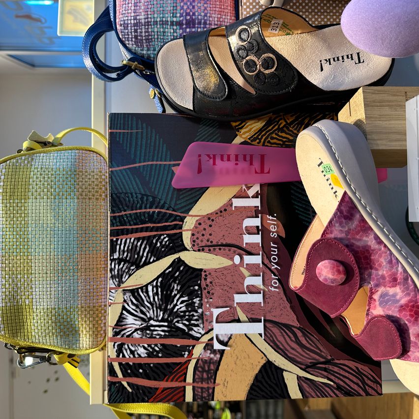 A display of colorful shoes, handbags, and accessories on a wooden surface. The shoes are in different styles and colors, while the handbags and accessories are in various designs.