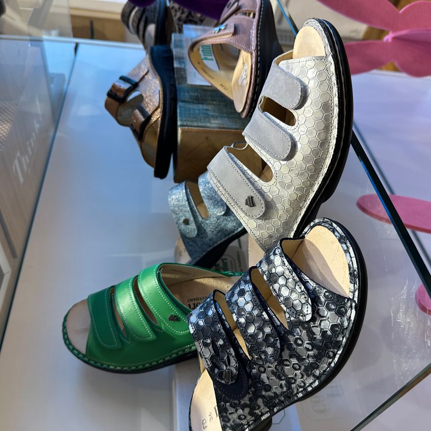 A glass display case shows multiple pairs of sandals in various colors. A green pair and a black pair are in the foreground.