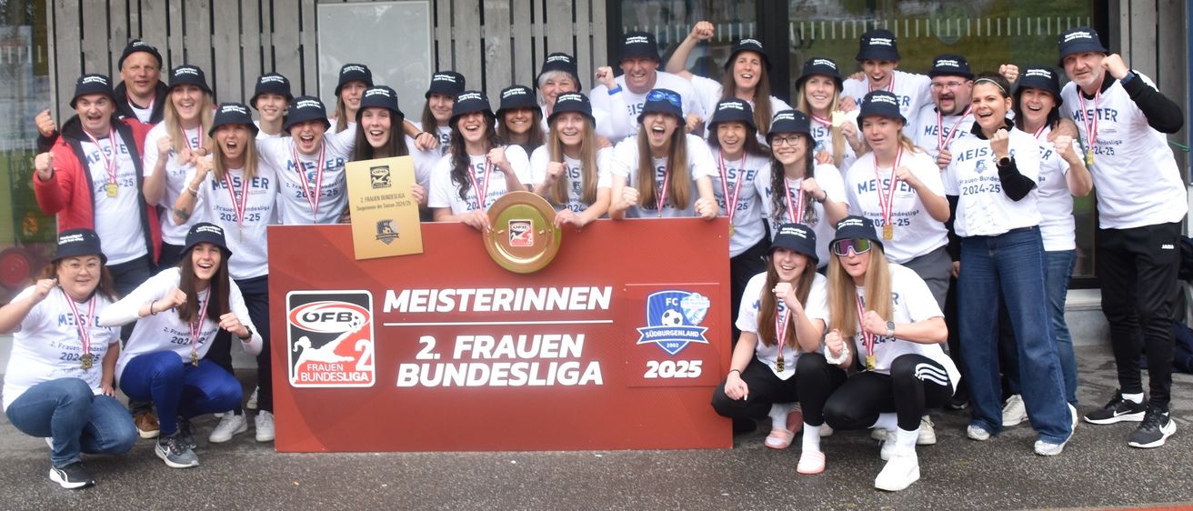 Eine Fußballmannschaft posiert mit einer Trophäe und einem Banner. Das Banner trägt die Aufschrift 'Meisterinnen 2. Frauen Bundesliga 2025'. Die Teammitglieder tragen Mützen und halten Medaillen.
