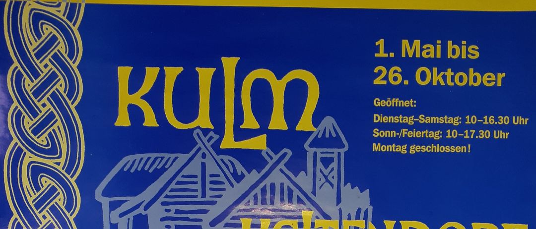 Deutsches Schild mit der Aufschrift 'In Stueck Anderswald, Kuelm'. Darunter ist eine Hausillustration. Der Text unter dem Haus lautet 'Keltendom'. Der Text auf der rechten Seite zeigt die Öffnungszeiten von 1. Mai bis 26. Oktober.