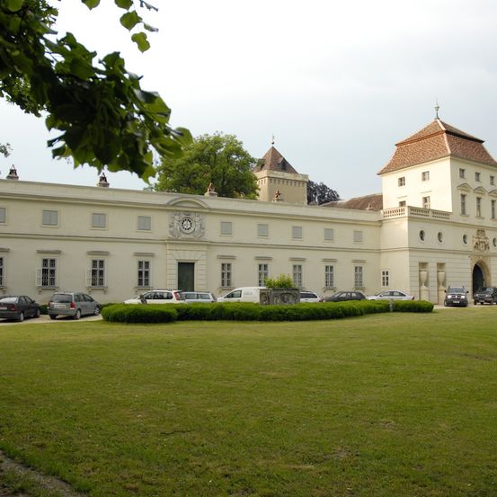 Ein großes, weißes klassisches Gebäude mit mehreren Autos davor. Es gibt einen großen grünen Rasen und Bäume im Hintergrund.