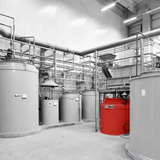 Industrieanlage mit großen zylindrischen Tanks und miteinander verbundenen Rohrleitungen. Die Behälter sind mit Nummern gekennzeichnet, wobei ein Tank rot gefärbt ist.