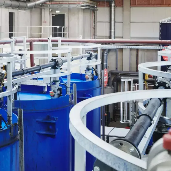 Eine industrielle Anlage mit blauen Tanks, Rohren und Maschinen. Die Tanks sind durch Rohre verbunden und werden von Metallkonstruktionen gestützt. Die Rohre sind an den Tanks befestigt und mit anderen Maschinen verbunden.