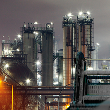 Ein Arbeiter in einem Chemiewerk bei Nacht, der eine Hochdruckreinigung verwendet und einen roten Helm sowie einen weißen Anzug trägt.