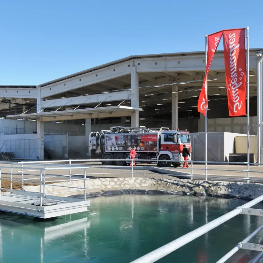 Ein roter Lkw ist vor einem großen Gebäude geparkt, an dem eine große Fahne hängt.