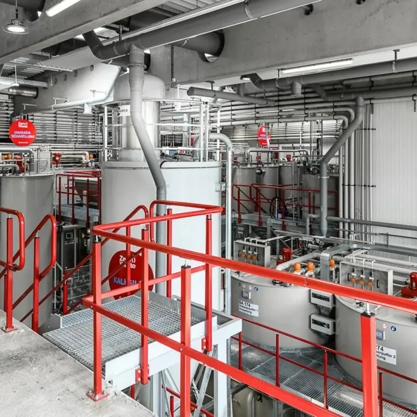 Industrieanlage mit mehreren großen Tanks, roten Handläufen und verschiedenen Rohren und Maschinen. Sicherheitsschilder sind an den Tanks sichtbar.