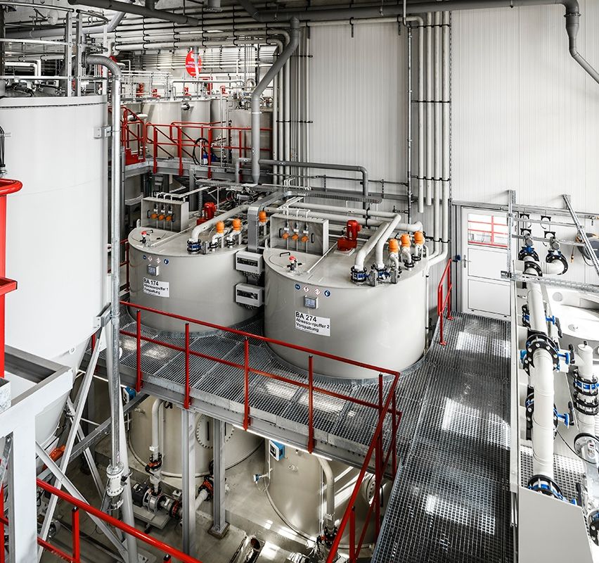Eine Industrieanlage mit großen zylindrischen Tanks, Rohrleitungen und Maschinen, mit einem roten Geländer auf einer Plattform über den Tanks.
