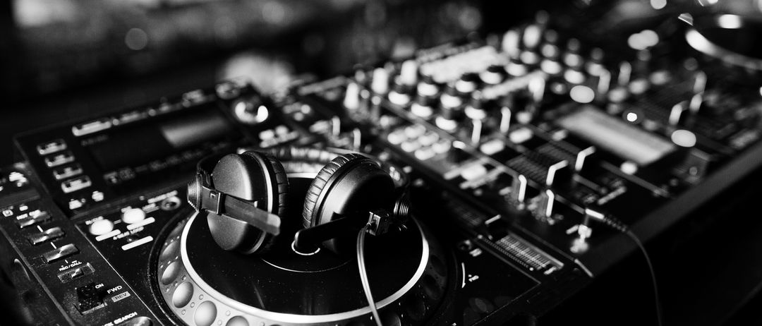 Ein Schwarz-Weiß-Foto eines DJ-Mixers mit Kopfhörern auf der Plattenspielerplatte und vielen Tasten und Reglern.