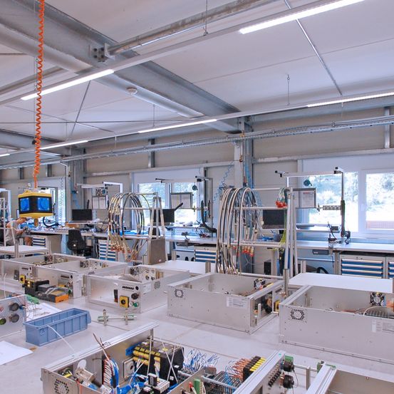 Ein überdachter Industriebetrieb mit mehreren Arbeitsplätzen, ausgestattet mit verschiedenen elektronischen Komponenten und Maschinen, beleuchtet durch Deckenleuchten.