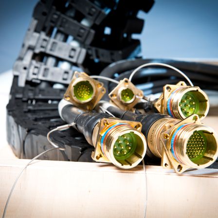 Mehrere vergoldete Steckverbinder mit grünen und schwarzen Kabeln liegen auf einer hölzernen Oberfläche mit schwarzem Hintergrund.