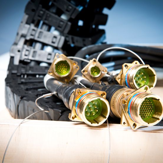 Mehrere vergoldete Steckverbinder mit grünen und schwarzen Kabeln liegen auf einer hölzernen Oberfläche mit schwarzem Hintergrund.