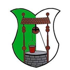 Ein heraldisches Emblem zeigt einen grünen Schild mit einem Brunnen in der Mitte. Der Brunnen hat einen roten Eimer und einen hölzernen Griff. Über dem Brunnen befindet sich eine Struktur mit einem Kreuz oben.