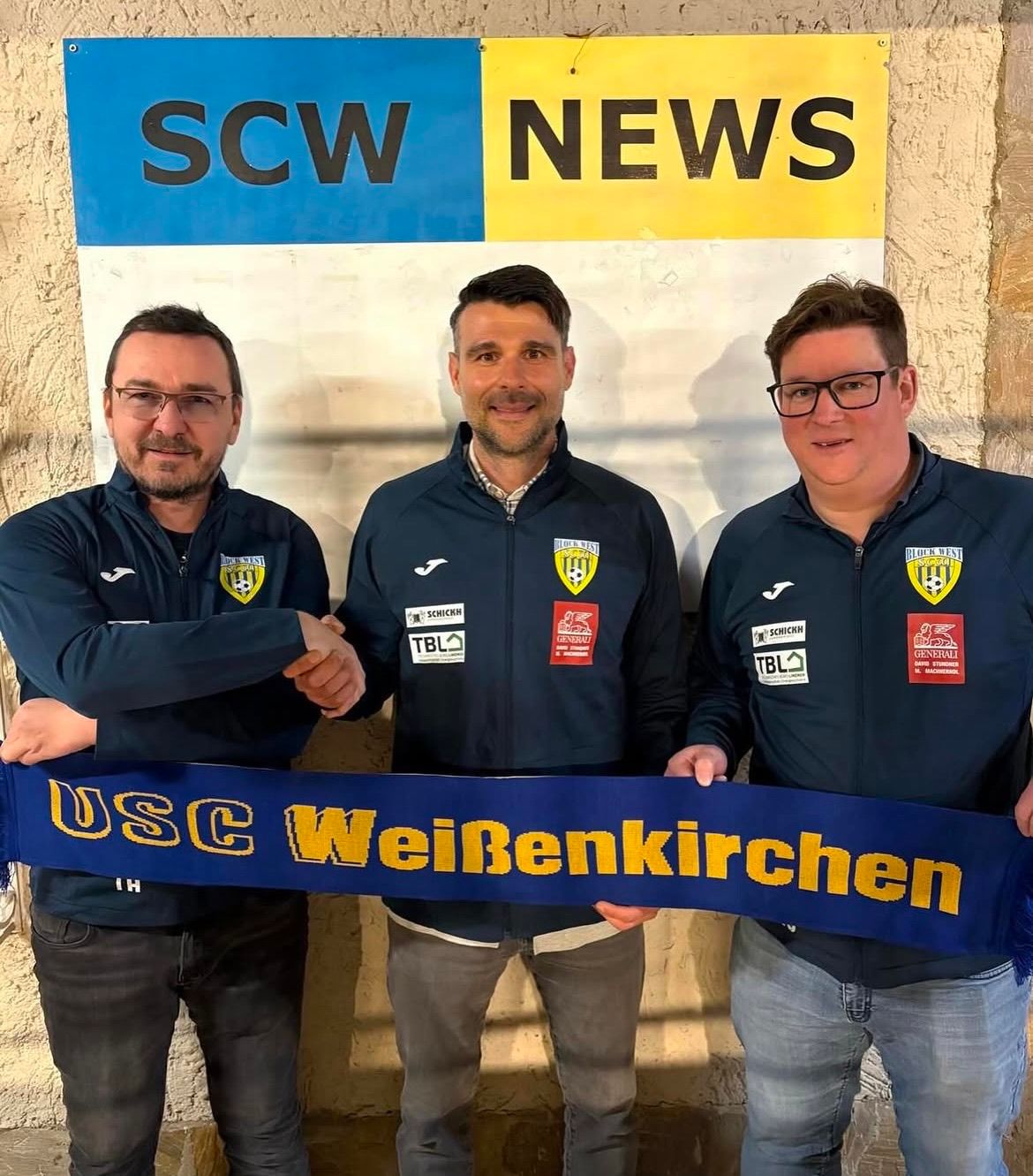 Drei Männer stehen hinter einem Banner mit der Aufschrift USC WeinBenKirchen und posieren für ein Foto vor einem SCW News-Schild. Sie tragen dunkelblaue Jacken mit Logos auf der Brust.