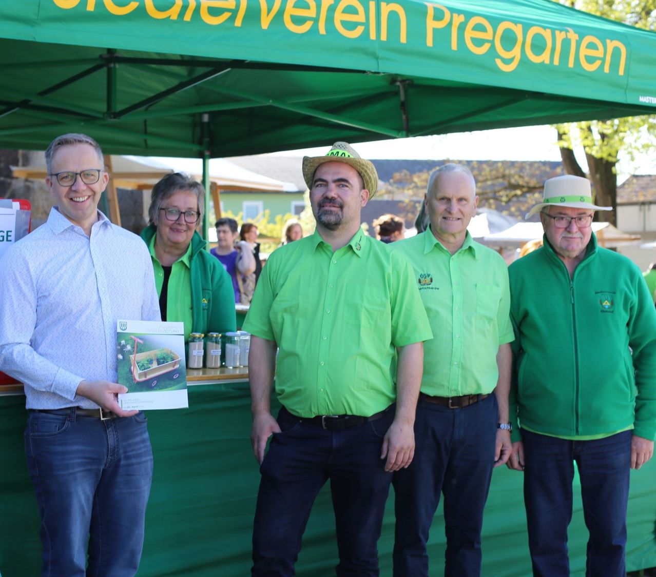 Fünf Personen stehen lächelnd unter einem Zelt. Der Mann links hält ein Büchlein. Hinter ihnen ist ein Tresen mit Gläsern. Das Zelt hat 'Verein Pregarten' darauf geschrieben.