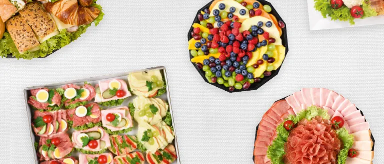 Eine Vielzahl von Speisen ist auf einem weißen Tisch angeordnet. Es gibt Sandwiches, Obst und Fleisch auf Tellern.