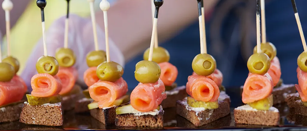 Eine Nahaufnahme von Canapes mit Lachs und Oliven auf Stöcken auf einem Tablett.