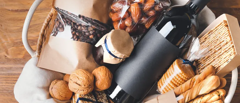 Ein Korb mit verschiedenen Snacks gefüllt, darunter Brot, Nüsse, Datteln und eine Flasche Wein, alles ordentlich auf einer Holzoberfläche angeordnet.