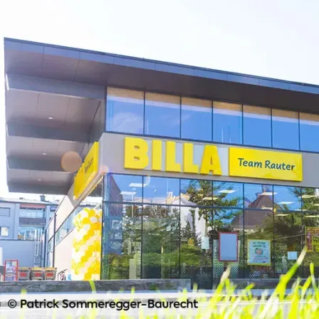 Die Vorderseite eines BILLA-Supermarkts mit gelben Luftballons und einem Schild, auf dem steht Team Rauter.