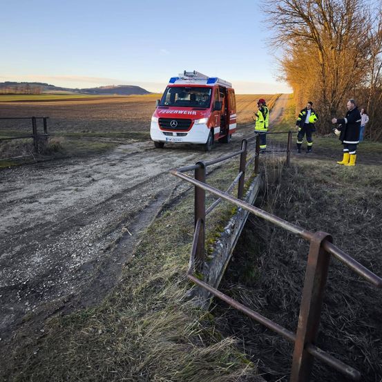 Ein Feuerwehrwagen steht auf einem Feldweg, drei Personen in Schutzkleidung stehen in der Nähe. Eine Person hält einen Feuerlöscher.