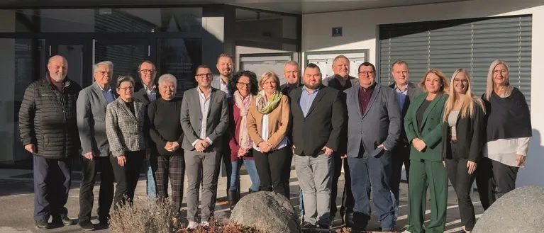 Eine Gruppe von Menschen in formeller Kleidung, die vor einem modern gestalteten Gebäude stehen und für ein Foto posieren.