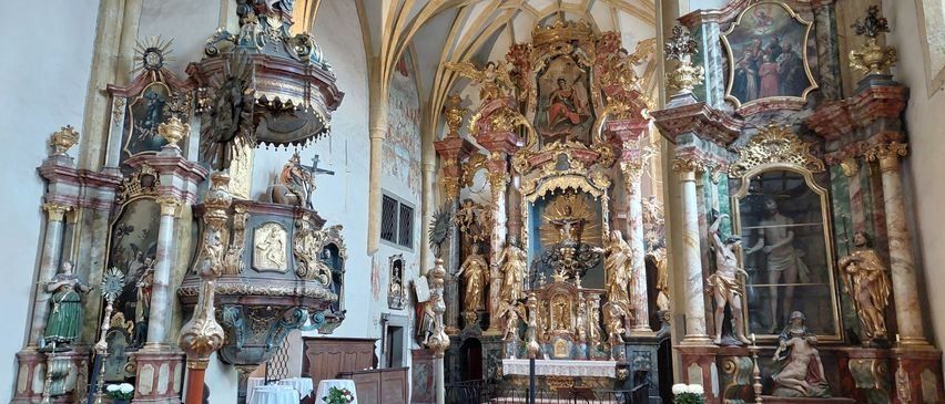 Ein barocker Altar in einer Kirche mit kunstvollen goldenen Statuen, aufwendigen Wandgemälden und dekorativen Bögen. Der Altar ist von goldenen Statuen umgeben, und die Wände sind mit Gemälden geschmückt.