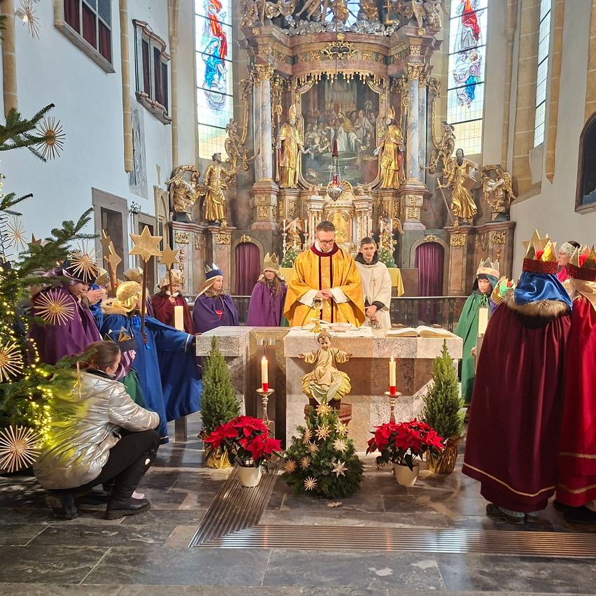 Eine religiöse Zeremonie in einer Kirche mit einem Priester und Chormitgliedern in traditionellen Kostümen, geschmückt mit Ornamenten und Kerzen.