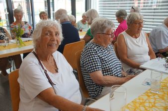 Eine Gruppe älterer Frauen sitzt an einem Tisch in einem Essbereich, lächelt und schaut in die Kamera.