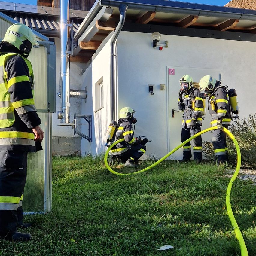 Feuerwehrleute in voller Montur üben vor einem Gebäude mit einer gelben Schlauchleitung auf dem Boden.