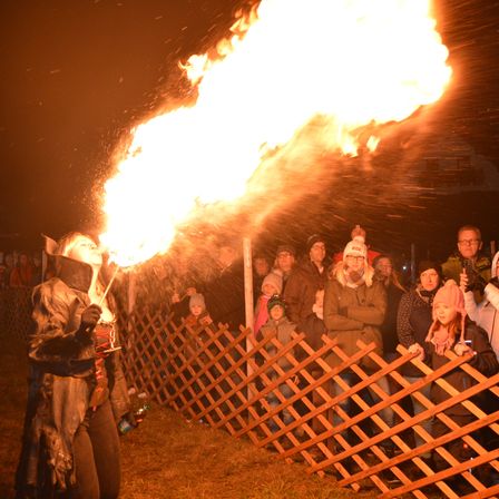 Eine Person bläst Feuer aus einer Fackel in einer Menschenmenge bei Nacht.