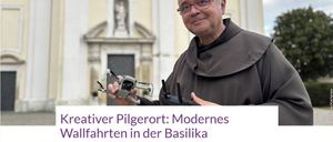 Ein Mann in einer Mönchskutte hält eine Drohne vor einer Kirche mit einer Statue über dem Eingang.