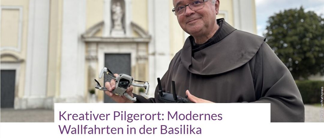 Ein Mann in einer Mönchskutte hält eine Drohne vor einer Kirche mit einer Statue über dem Eingang.