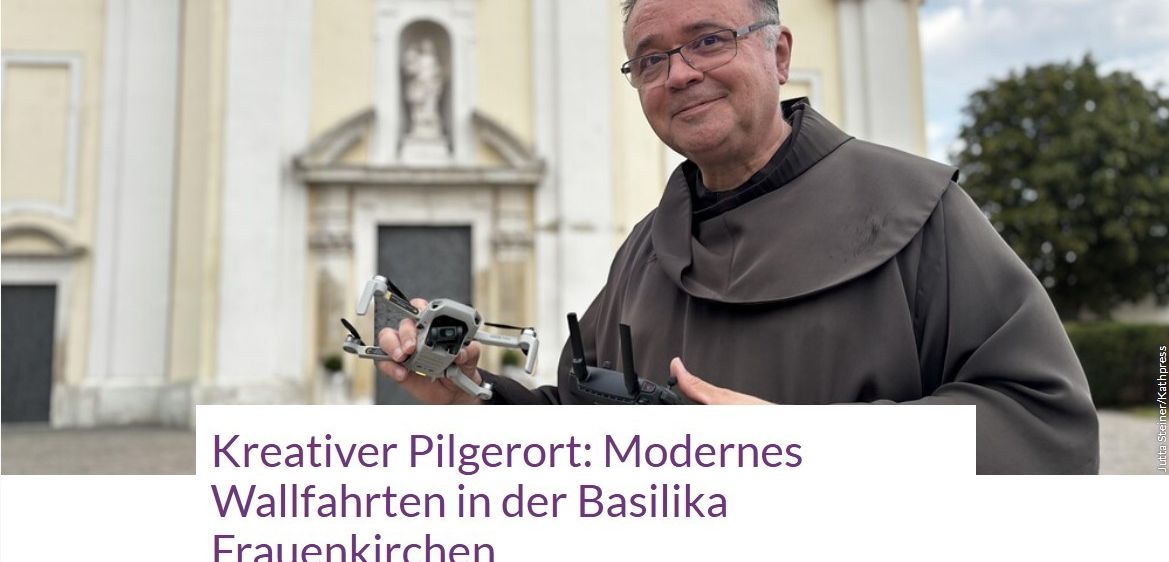 Ein Mann in einer Mönchskutte hält eine Drohne vor einer Kirche mit einer Statue über dem Eingang.