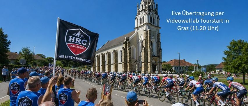 Cycling race with cyclists and supporters in front of a church. The event is the Tour of Austria.