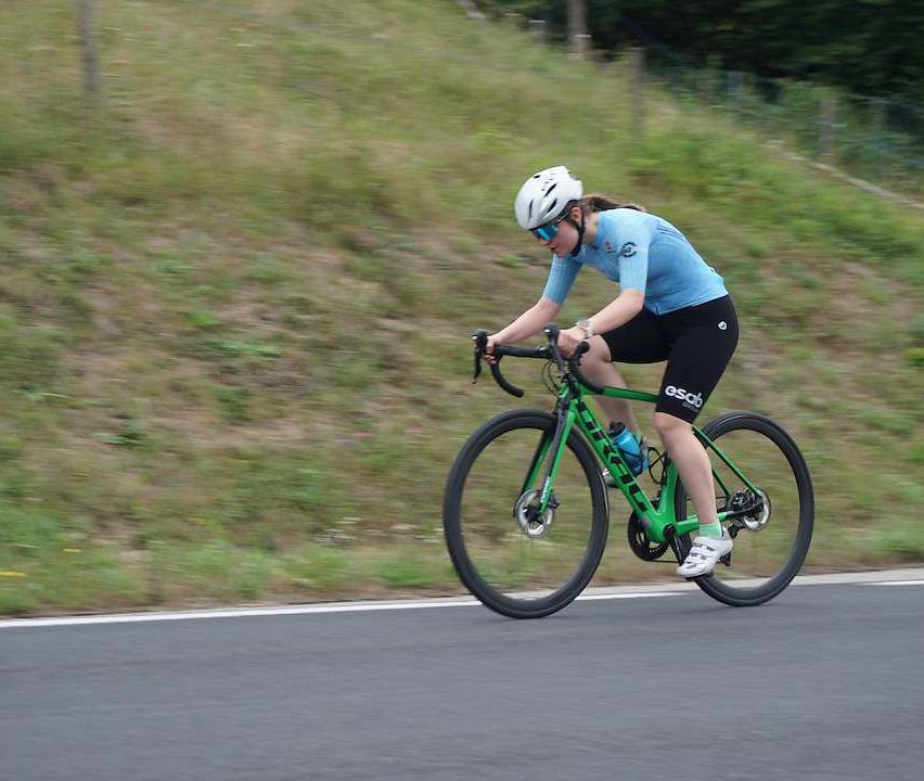 Eine Frau in einem blauen Shirt und schwarzen Shorts fährt ein grünes Fahrrad die Straße hinunter.