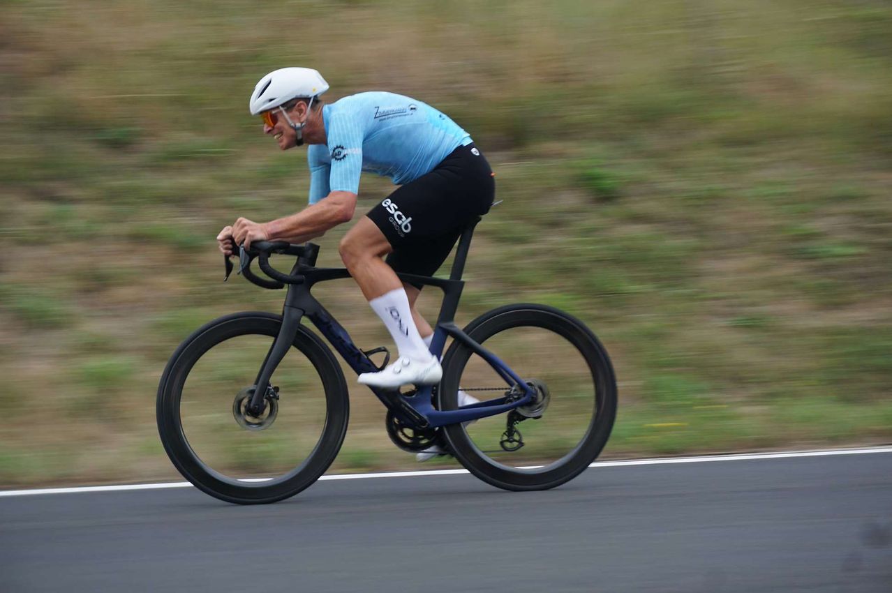 Ein Radfahrer in einem blauen Trikot fährt ein Hochleistungsrad auf einer Straße und fängt die Bewegung mit einem verwischten Hintergrund ein.