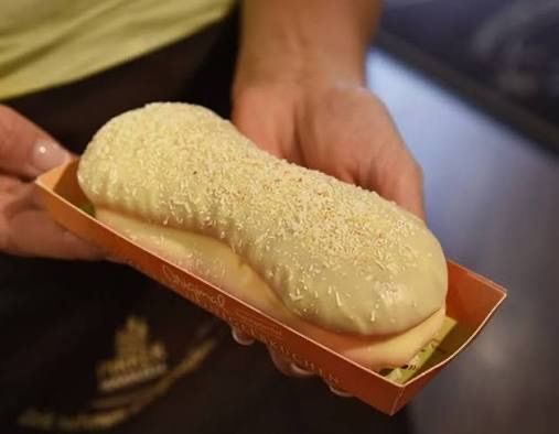 A person holds a pastry in a red box, covered in white icing and sprinkles.