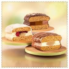 Three ice cream sandwiches on wooden boards. One has white cream and a raspberry, another has chocolate, and the last one has a chocolate and vanilla combination.