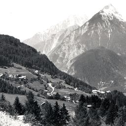 Ein Schwarz-Weiß-Foto einer Berglandschaft mit einem kleinen Dorf im Tal darunter.
