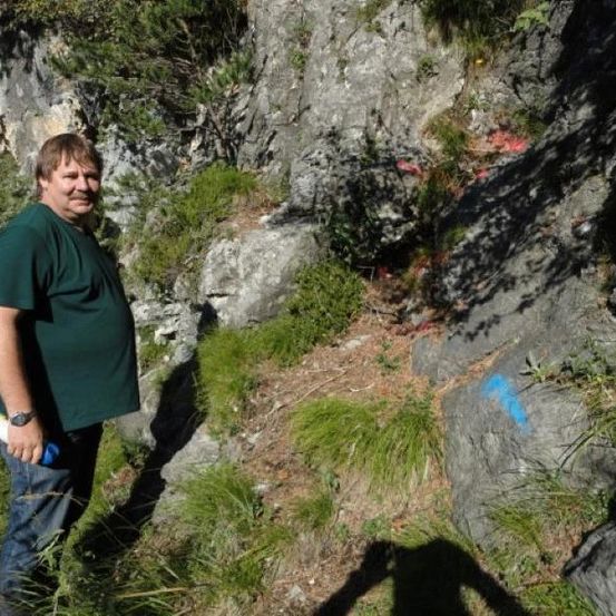 Ein Mann in einem grünen T-Shirt und Jeans steht auf einem felsigen Hang mit einem blauen Marker auf einem Felsen.