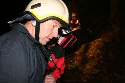 Ein Feuerwehrmann mit weißem Helm und schwarzem Jacke schaut in einem dunklen Bereich nach unten.
