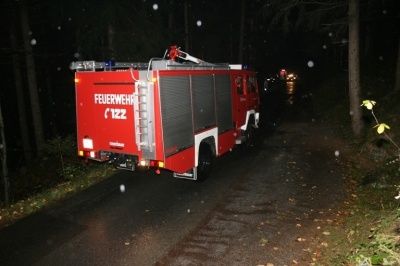 Ein roter Feuerwehrwagen fährt nachts auf einer dunklen, verschneiten Straße. Der Wagen hat das Wort 'Feuerwehr' an der Seite und eine Leiter obenauf.