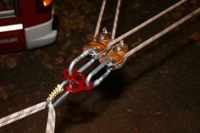 Ein Nahaufnahme eines roten und silbernen Karabiners, der mit einem weißen Seil verbunden ist, möglicherweise zum Klettern oder zur Sicherung eines Fahrzeugs.