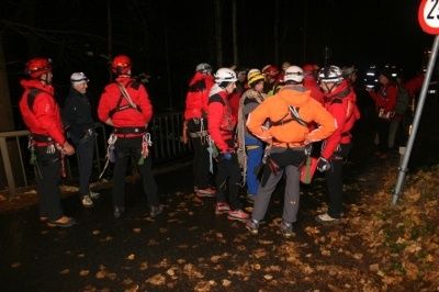 Eine Gruppe von Menschen in roten Jacken und Helmen steht nachts in einer Reihe auf der Straße. Sie scheinen sich auf eine Aktivität vorzubereiten.