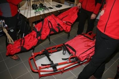 Zwei Personen in roten Jacken halten eine rote Trage mit roter Abdeckung, möglicherweise in Vorbereitung auf einen Notfall.