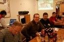 Eine Gruppe von Männern sitzt um einen Tisch herum mit verschiedenen Flaschen und einer Projektionsleinwand im Hintergrund.