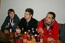 Drei Männer sitzen an einem Tisch mit verschiedenen Flaschen und Dosen vor ihnen. Der Mann auf der linken Seite hält eine Flasche, der Mann in der Mitte hat seine Hände auf dem Tisch und der Mann rechts schaut in die Kamera.