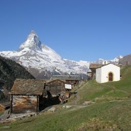 Ein kleines Dorf mit Holzhäusern und einer Kirche am Hang mit dem Matterhorn im Hintergrund.