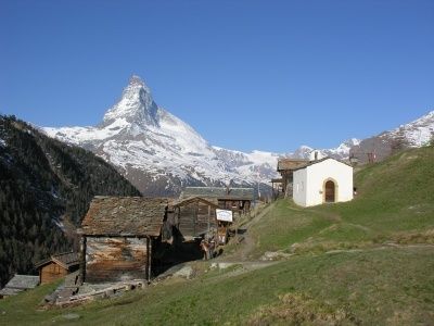 Ein kleines Dorf mit Holzhäusern und einer Kirche am Hang mit dem Matterhorn im Hintergrund.